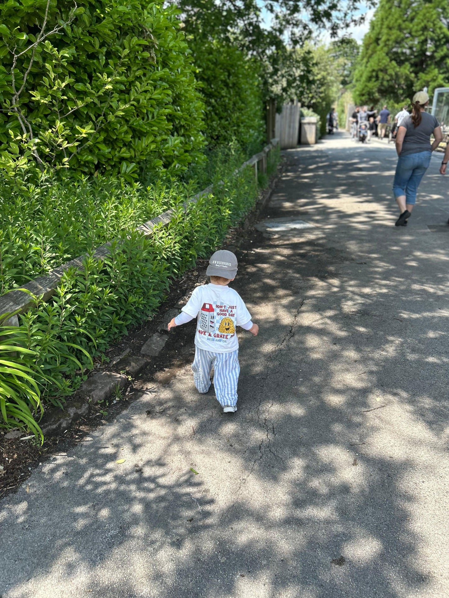 Toddler in Beck and Co. streetwear graphic tee and striped pants walking outdoors on a sunny path