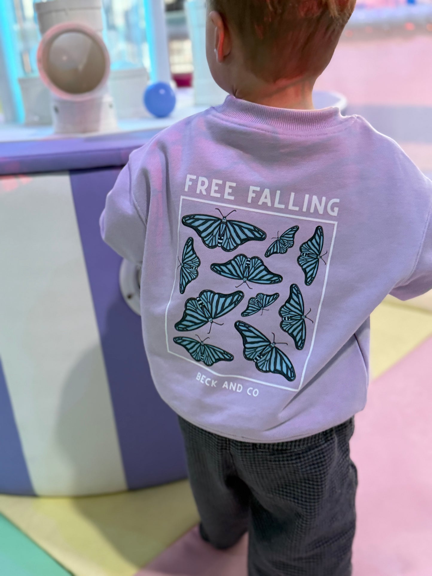 Child wearing a white hoodie with butterfly design and 'Free Falling' text in an indoor setting.