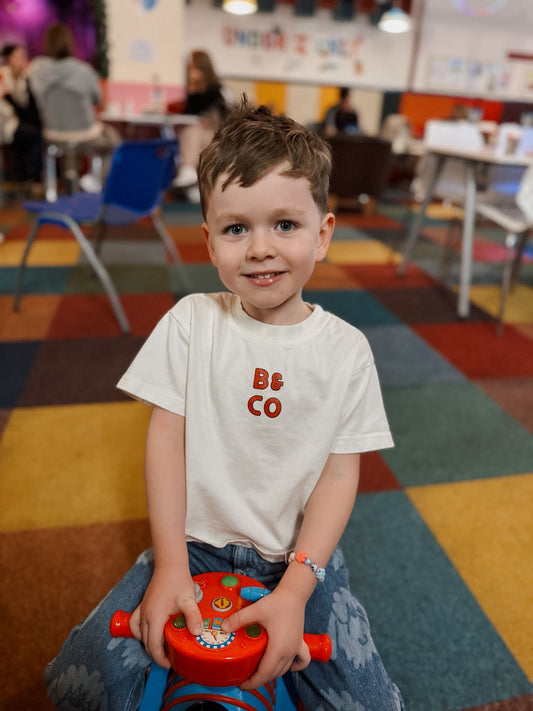 Child sitting on a red toy stool in a colorful room with people in the background