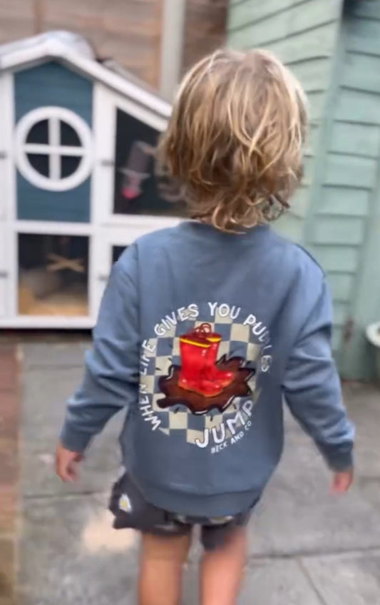 Child wearing a blue sweatshirt with a graphic design, standing in front of a playhouse.