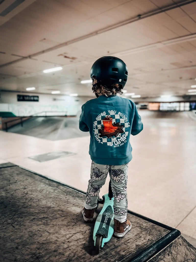 Child in Beck and Co. kids streetwear on scooter at skate park, wearing helmet and graphic sweatshirt