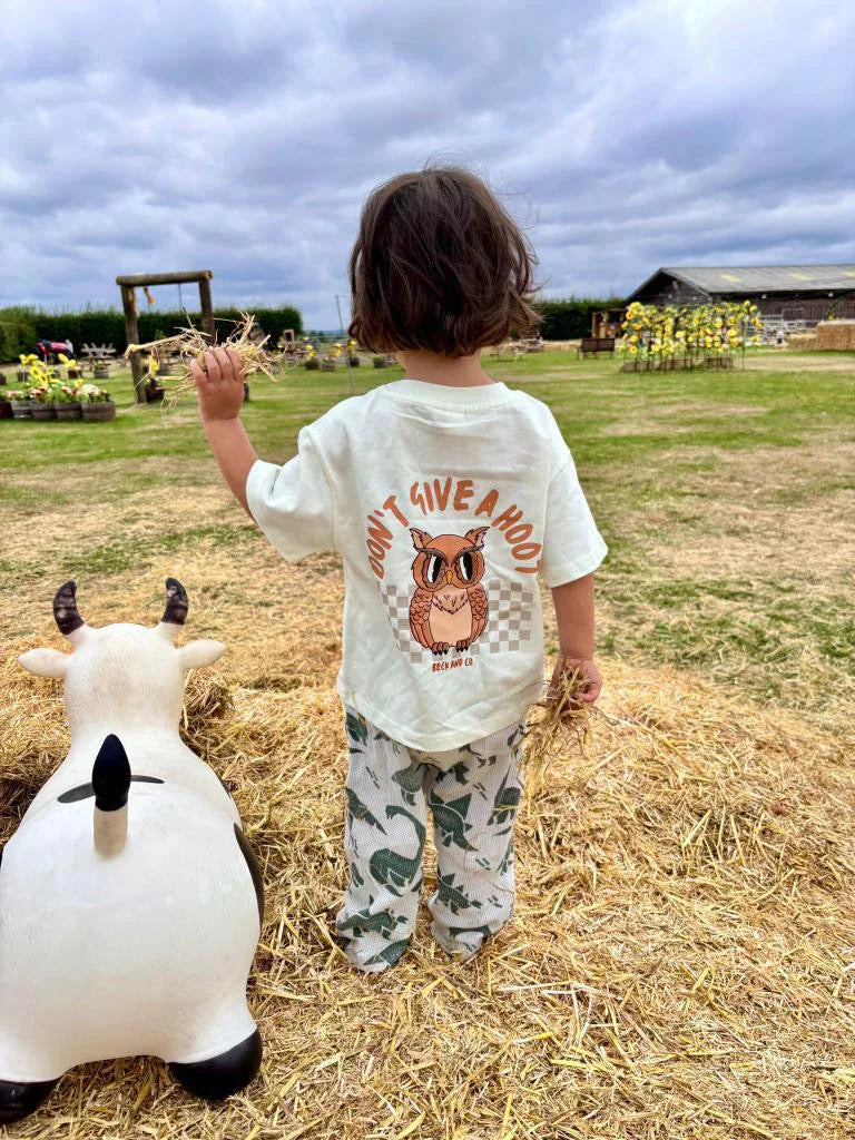 Child in Beck and Co. streetwear owl tee standing on hay beside cow toy in a farm setting.
