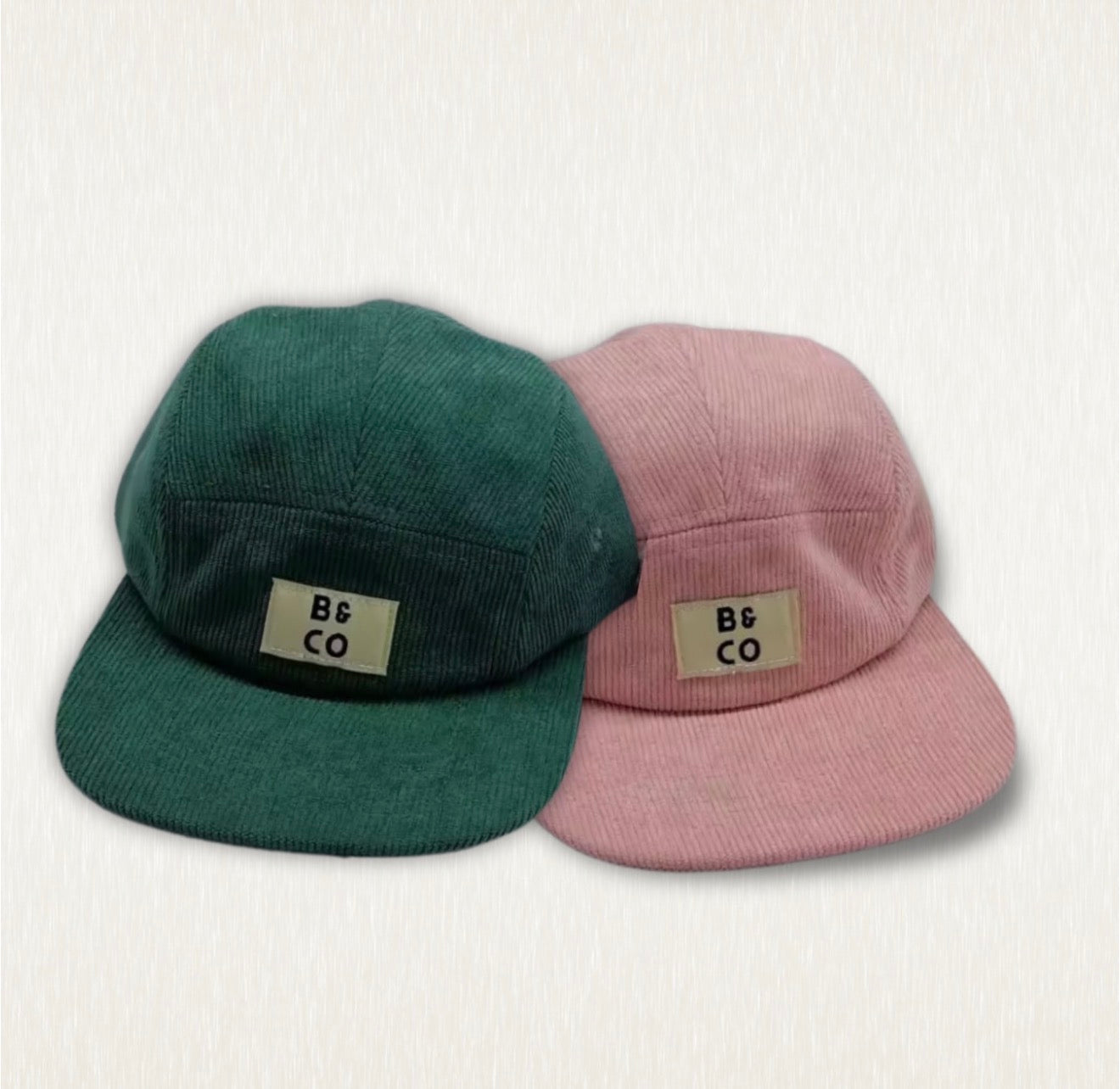 Two caps, one green and one pink, with 'B&CO' label on a light gray background.