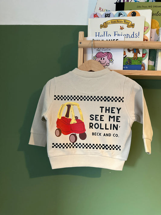Beck and Co. children’s sweatshirt with toy car print and skater style, hanging by kids’ books