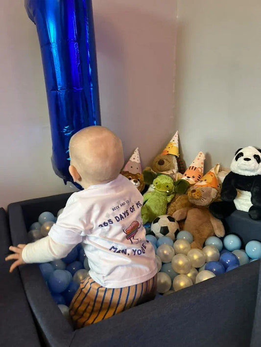 Toddler in Beck and Co. streetwear plays in a ball pit with stuffed animals and party hats