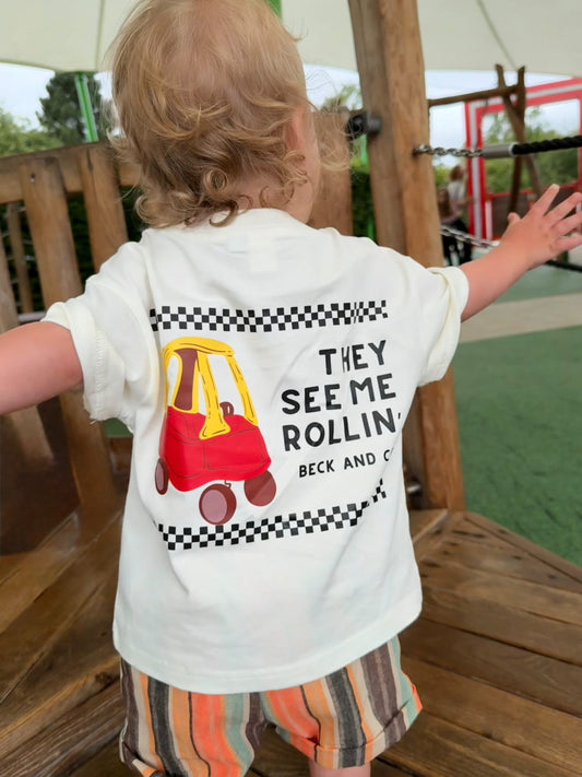 Child wearing a white t-shirt with a graphic and text, standing on a wooden deck.