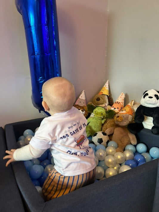 Child in cropped white t-shirt with graphic design playing with toys and balloons in a ball pit