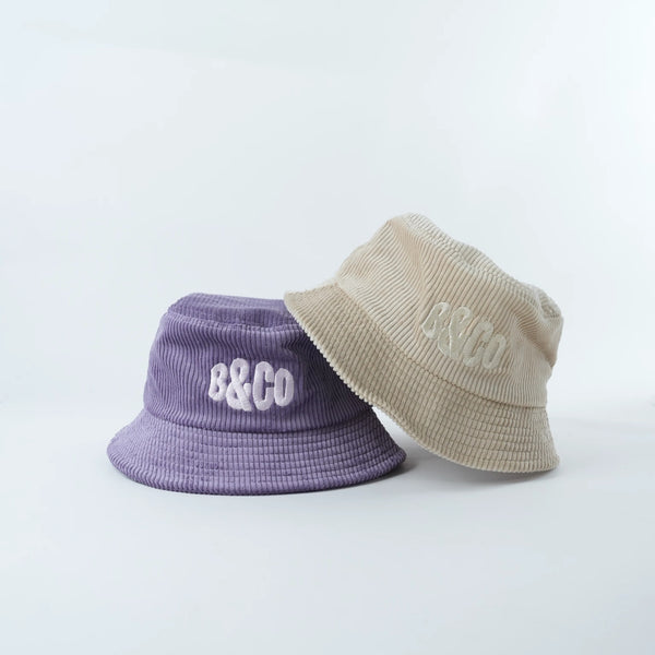Two bucket hats, one purple and one beige, with 'B&Co' branding on a light gray background.