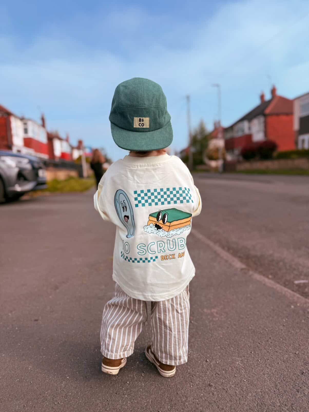 Child wearing a white shirt with graphics and text, standing on a residential street.