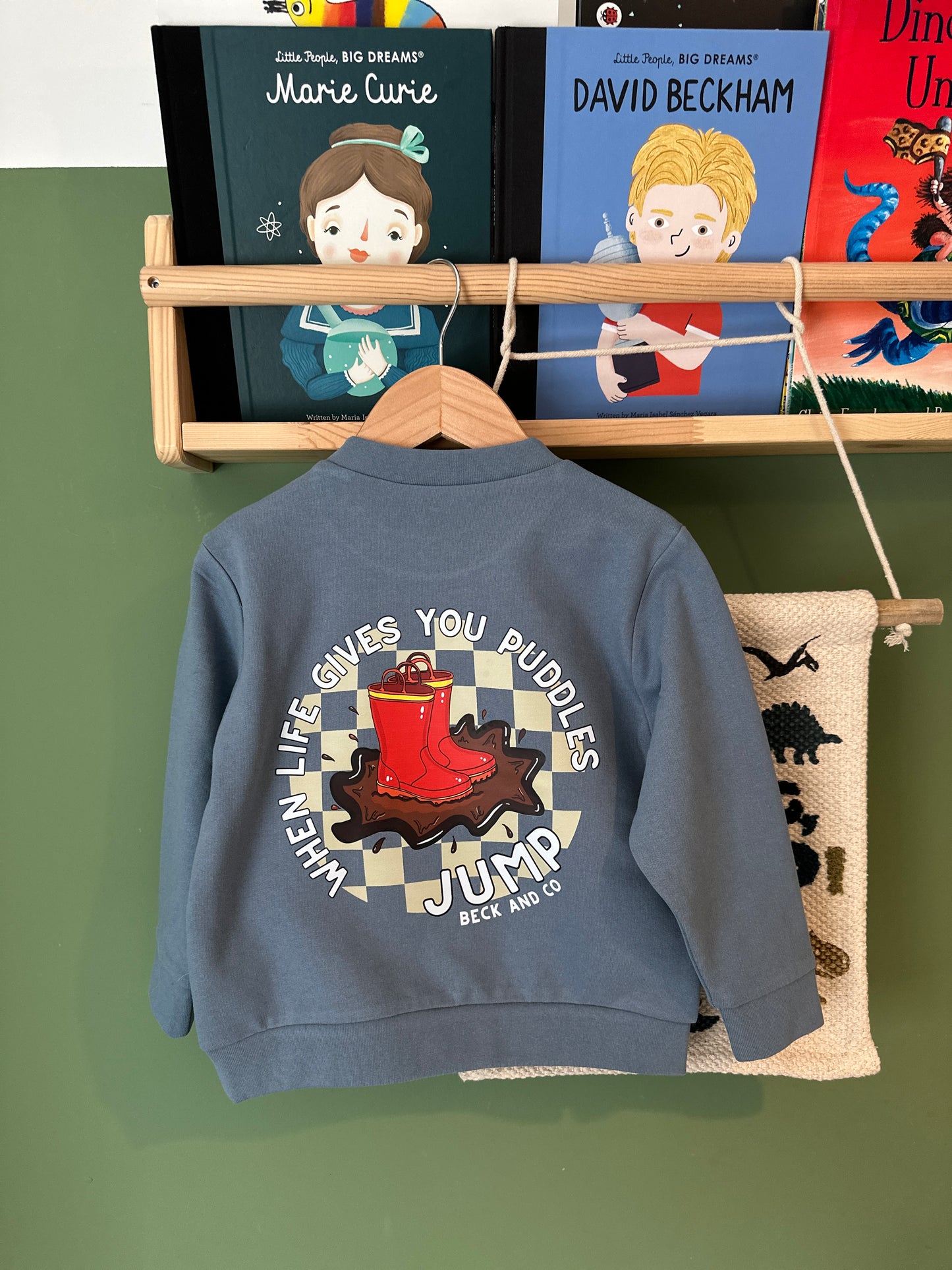 Blue sweatshirt with graphic design on a hanger against a green background with books.