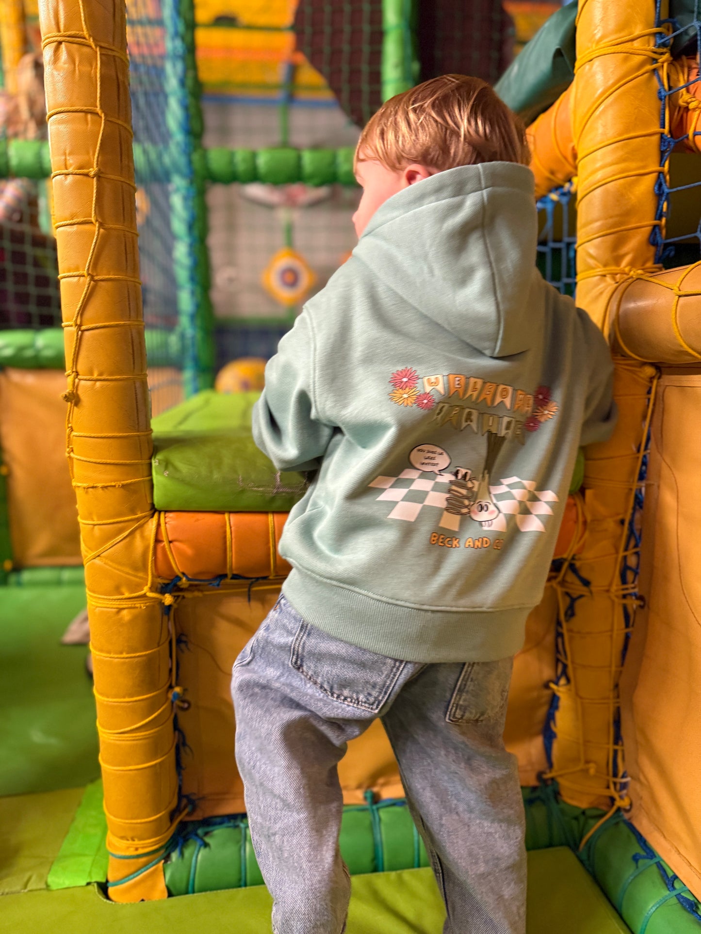 Child in a light green hoodie with colorful graphics in an indoor play area.