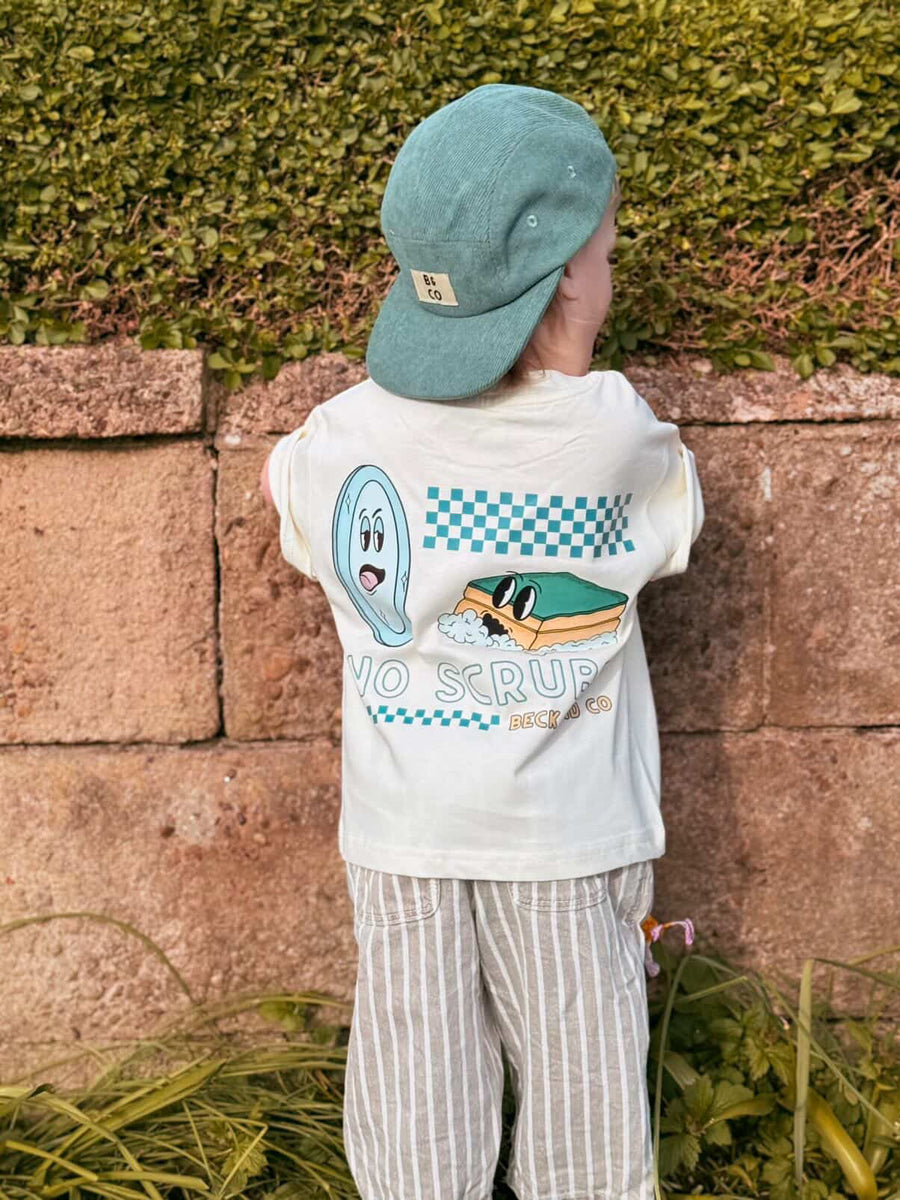 Child wearing a white shirt with graphics and text, standing against a stone wall with greenery.