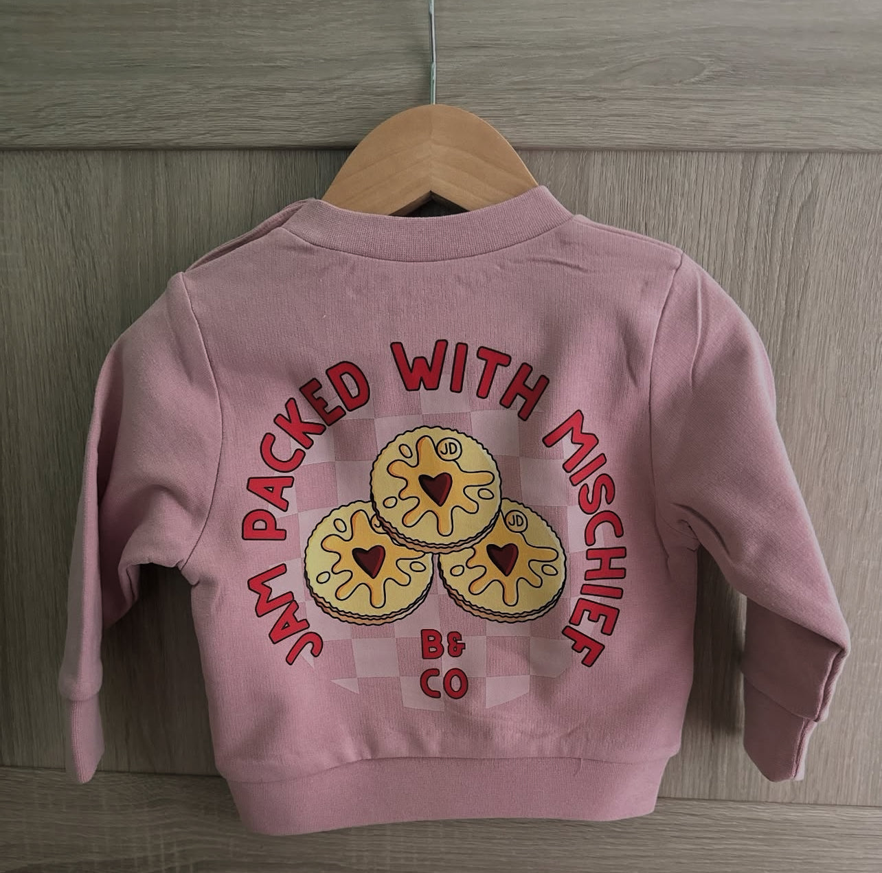 Pink children's jacket with cookie design and text on a wooden background