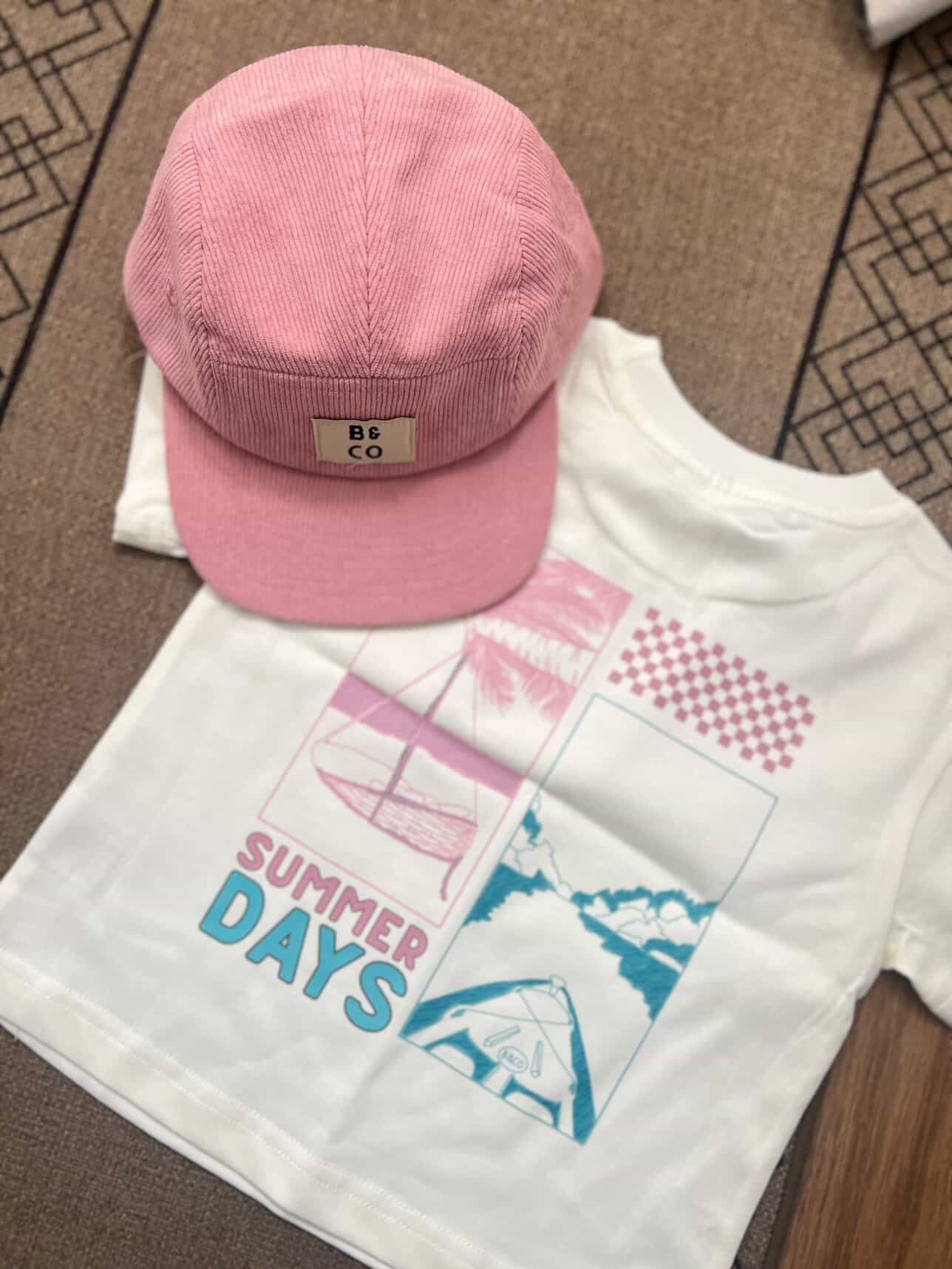 Pink cap and white t-shirt with 'Summer Days' design on a patterned surface