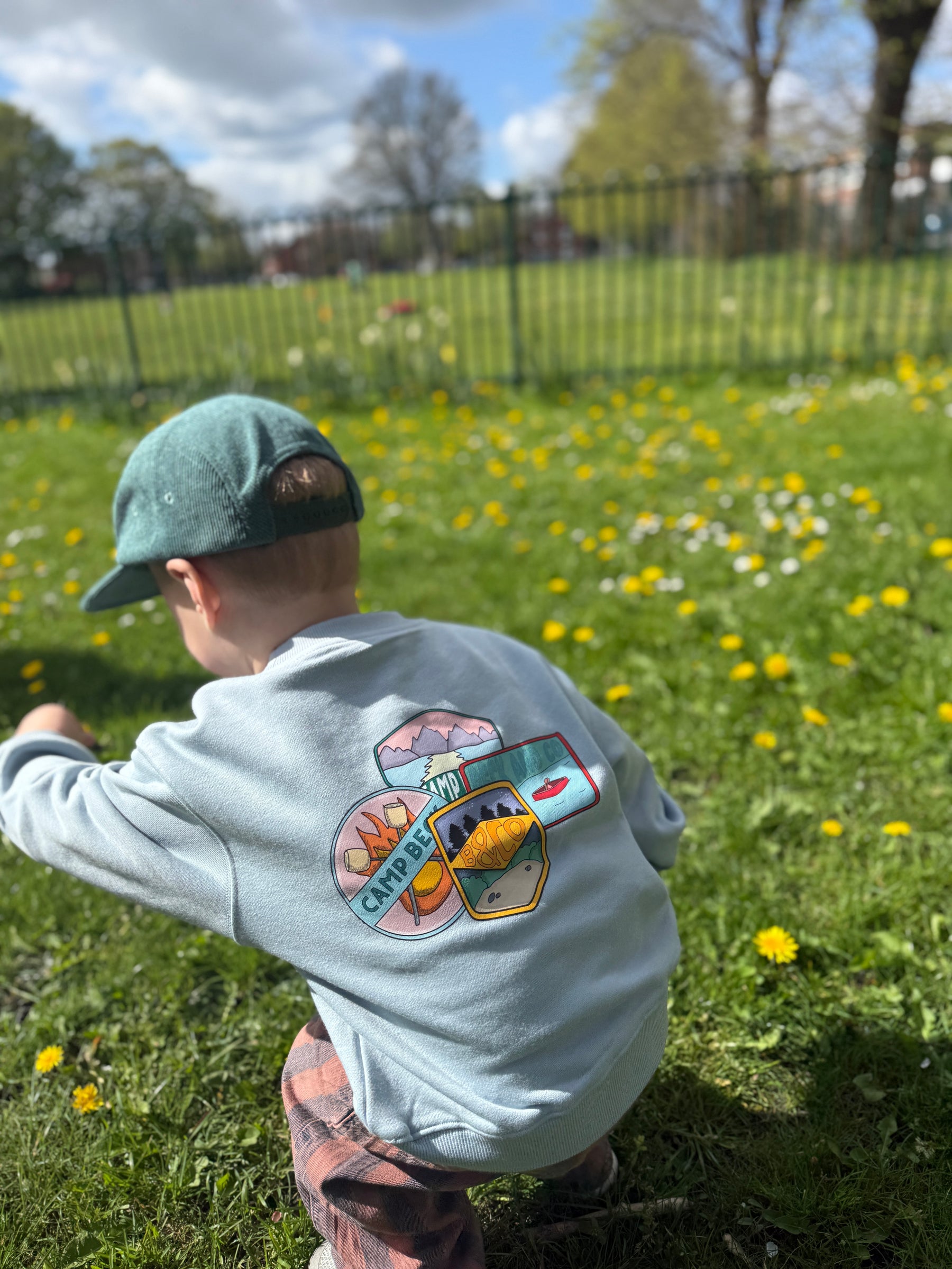 Child wearing a blue heavyweight sweatshirt with a colorful camping design in a park setting