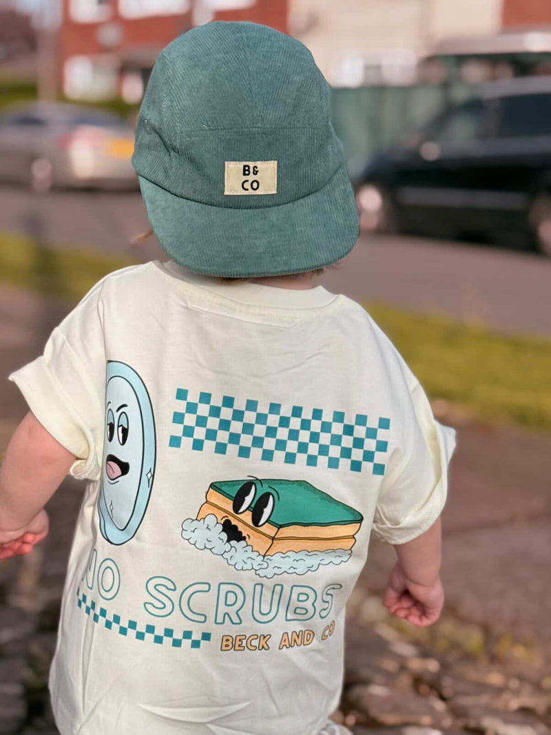 Child wearing a shirt with a cartoon design and a cap, standing on a street.