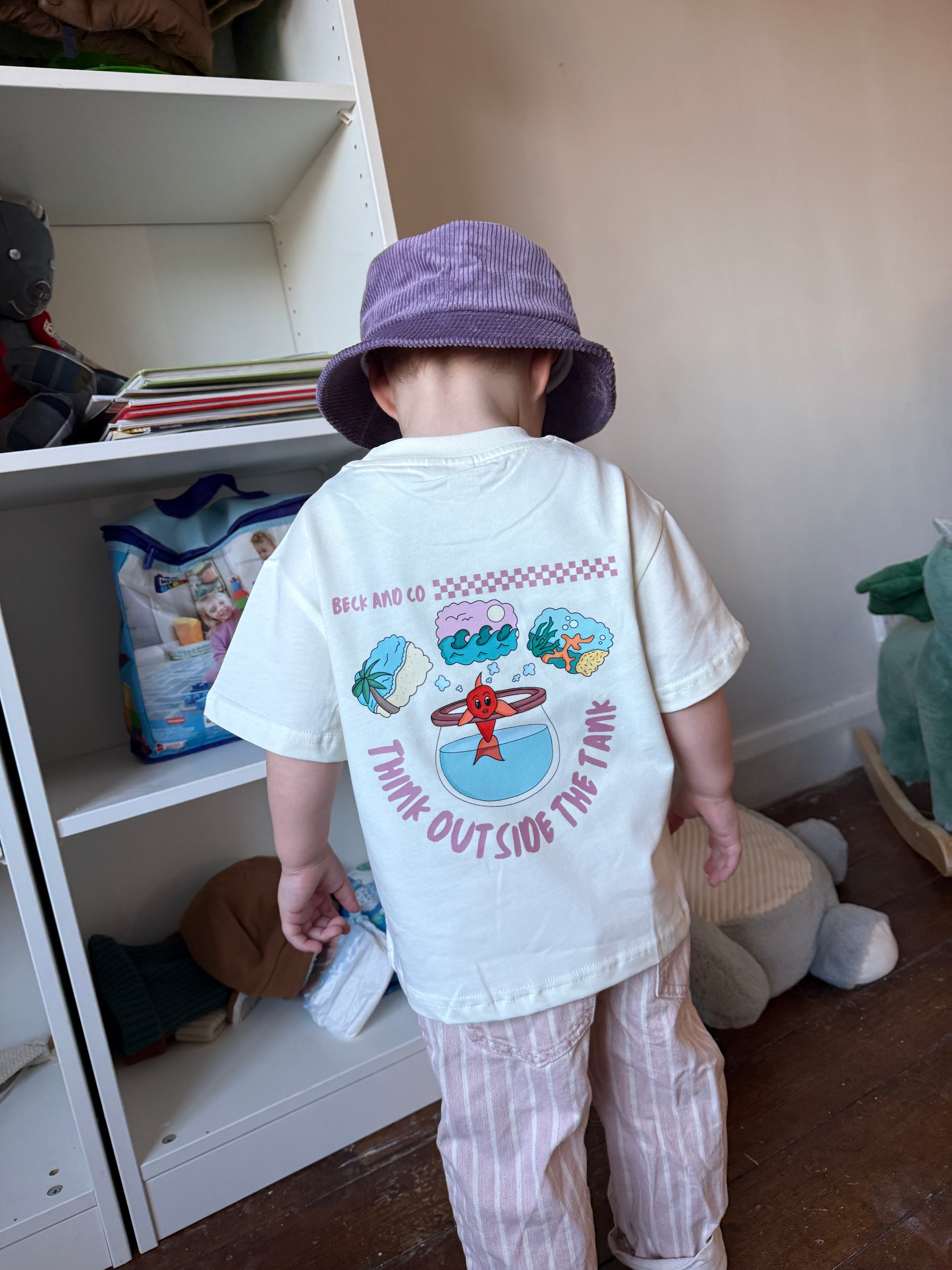 Child wearing a graphic t-shirt with a cartoon design, standing in front of a white cabinet.