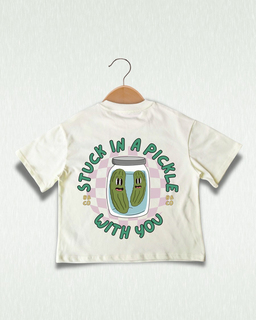 Children's t-shirt with pickle graphic and text on a hanger against a light background