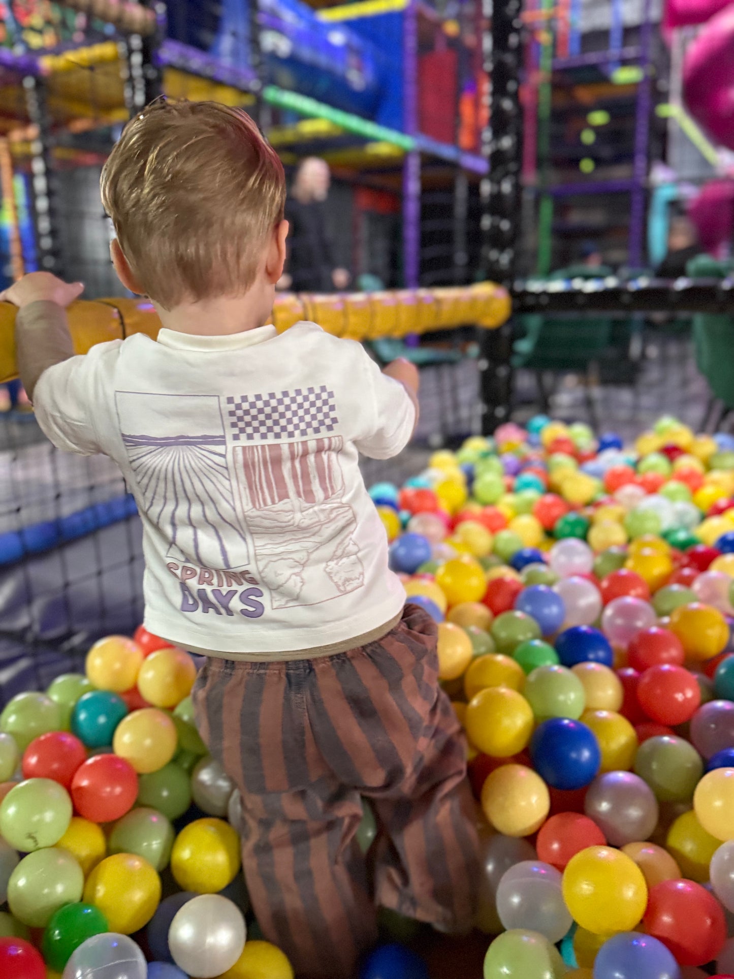 Child in a ball pit at an indoor playground with colorful balls and play structures.