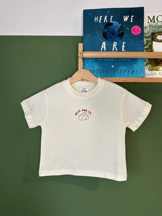 Beck and Co. kids white streetwear t-shirt with cheese logo, hanging on green wall