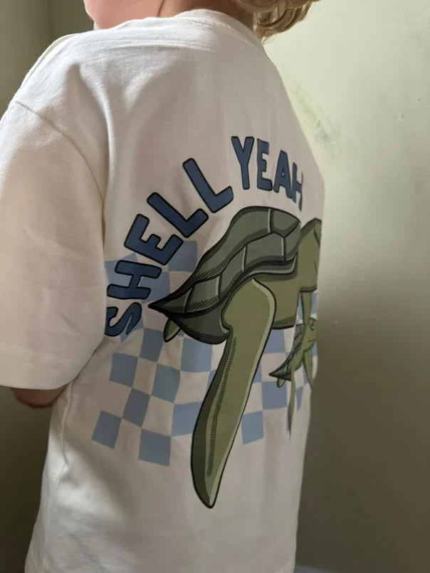Child wearing a white t-shirt with 'Shell Yeah' and a graphic design on the back.