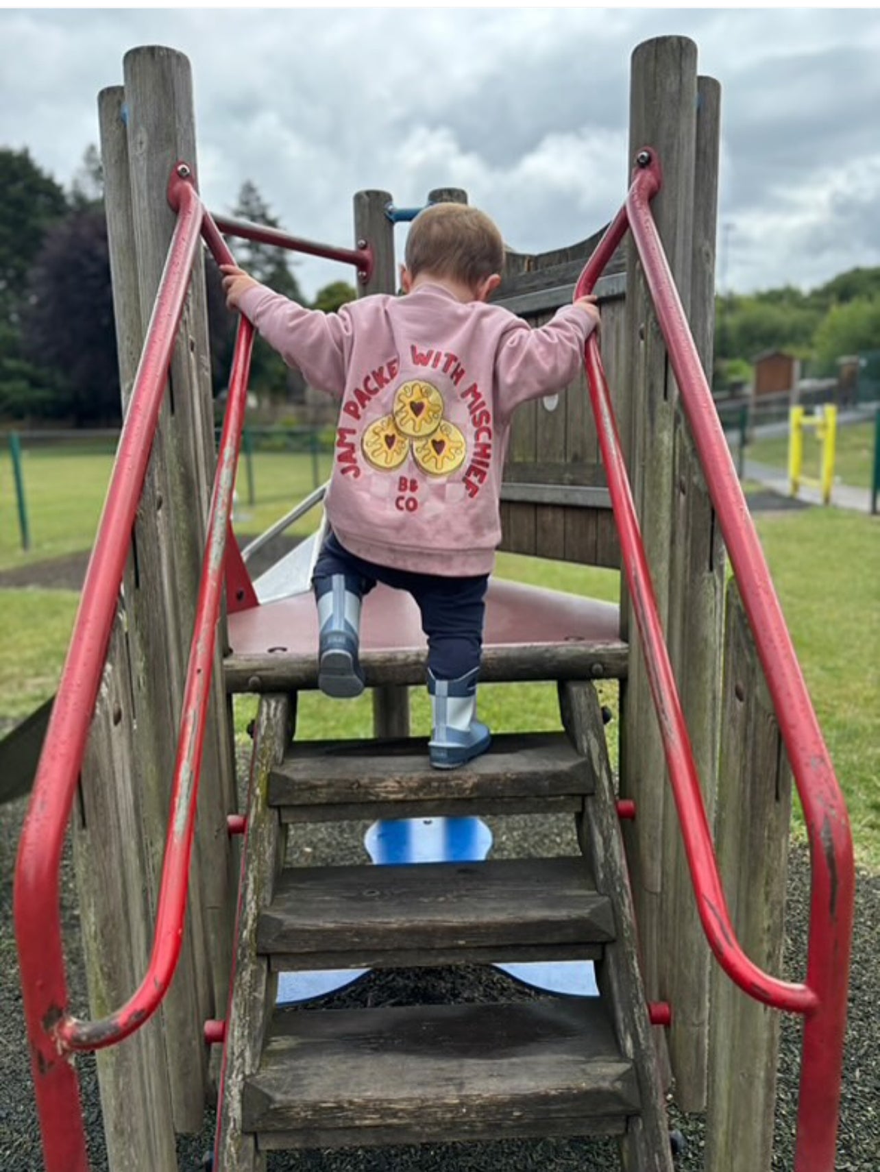 Child climbing a playground slide with a pink sweatshirt featuring jammie biscuits.