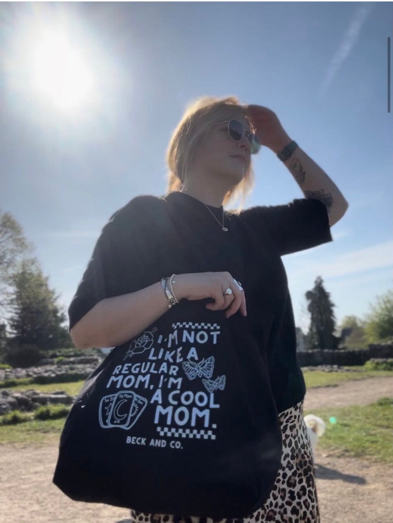 Person wearing a black tote with a printed design outdoors on a sunny day.