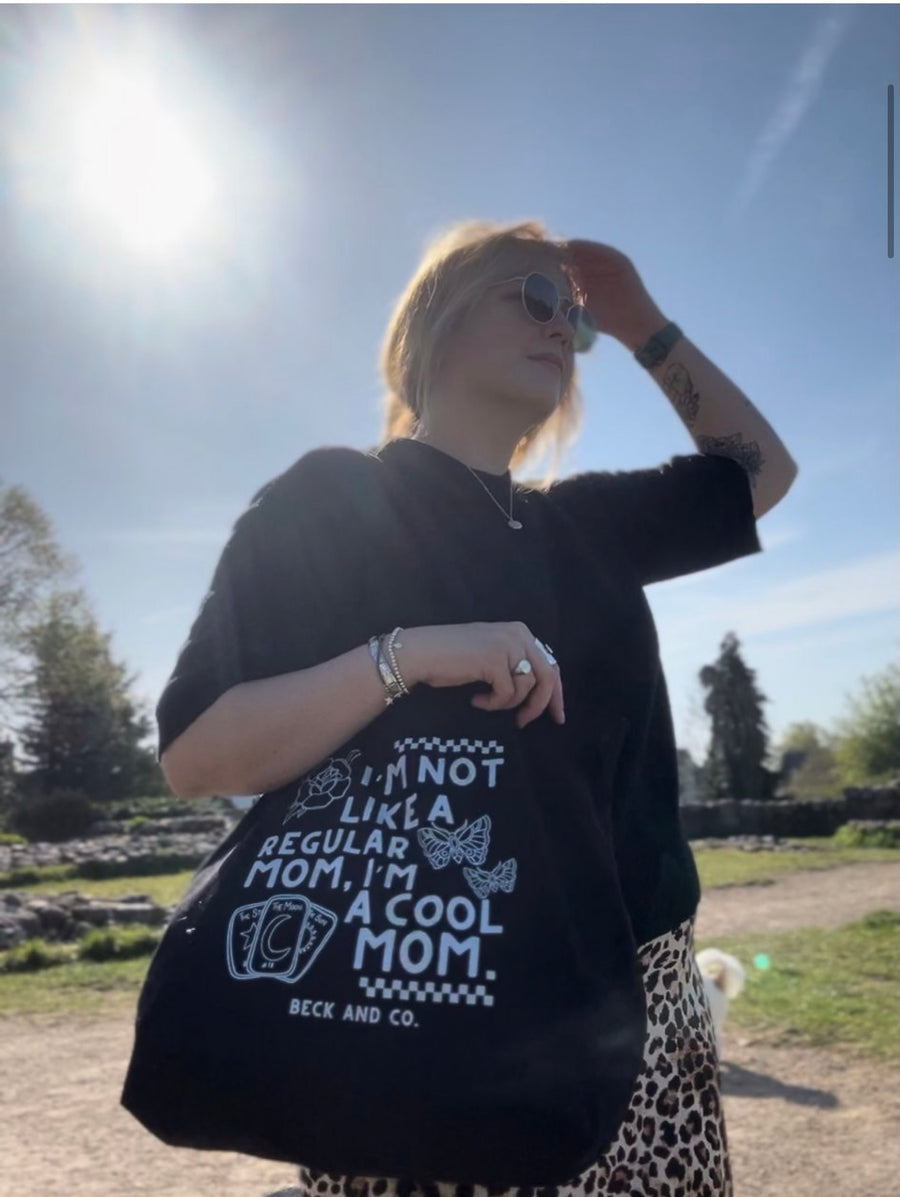 Person wearing a black tote with a printed design outdoors on a sunny day.